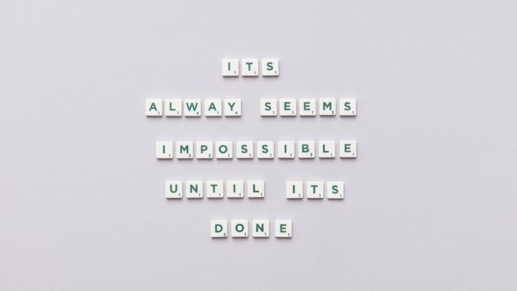 Motivational quote 'It always seems impossible until it's done' in Scrabble tiles.